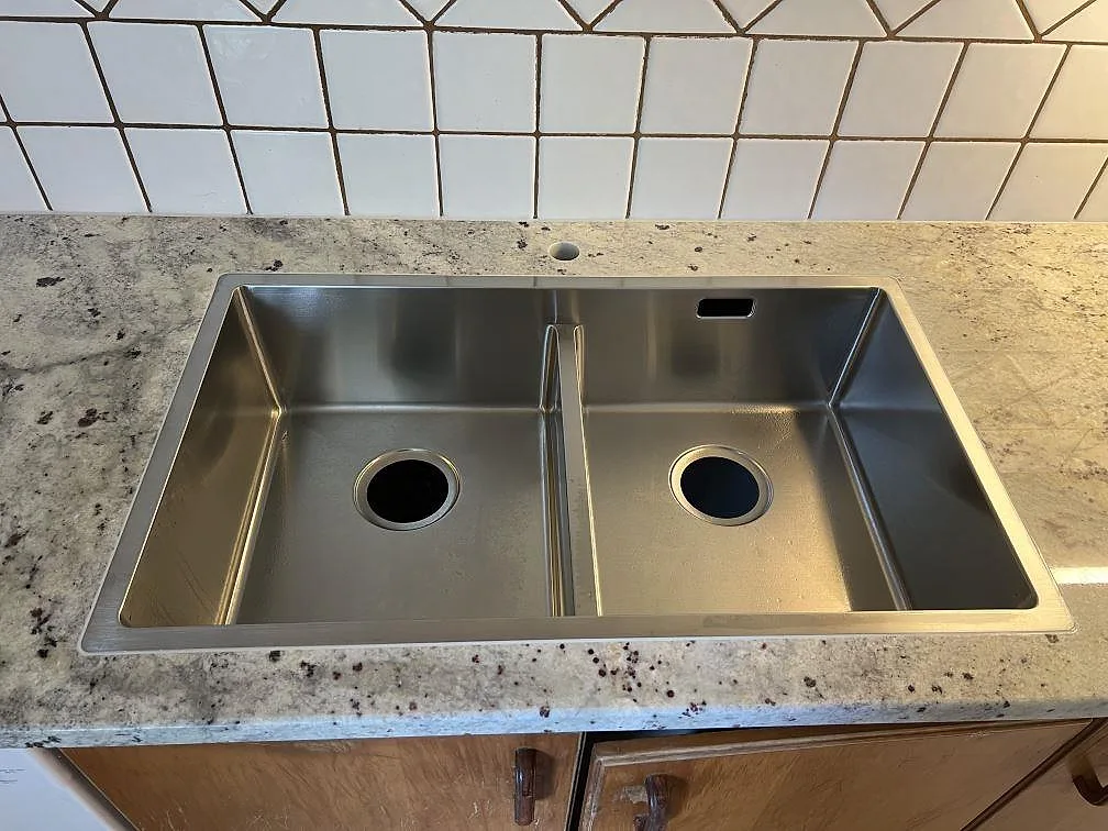 Underlimmad rostfri dubbelho i en polerad köksbänkskiva av Antique White granit i Svedala.