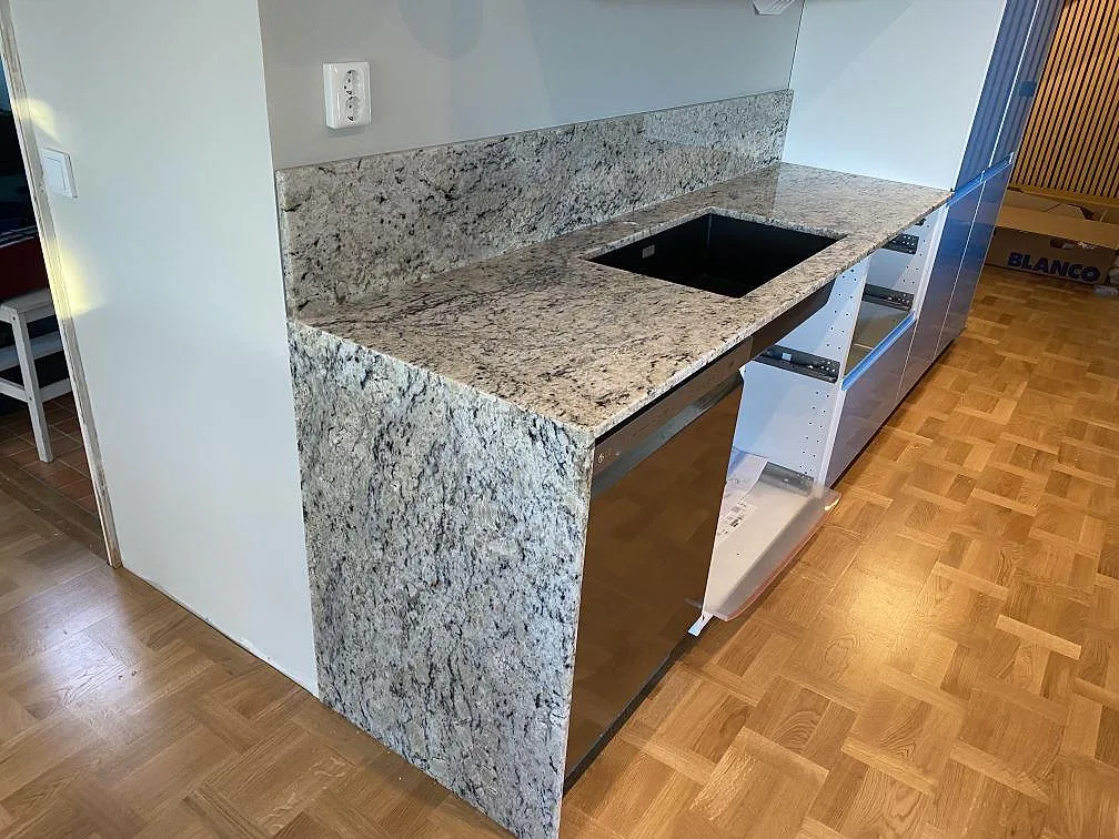 Polerad köksbänkskiva i Antique White granit med stänkkant och hällurtag i ett kök under montering i Svedala.