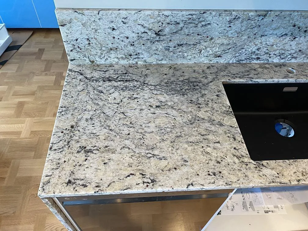 Detalj av polerad Antique White granit med svart diskho, blandarhål och uppvikt stänkkant i Svedala.