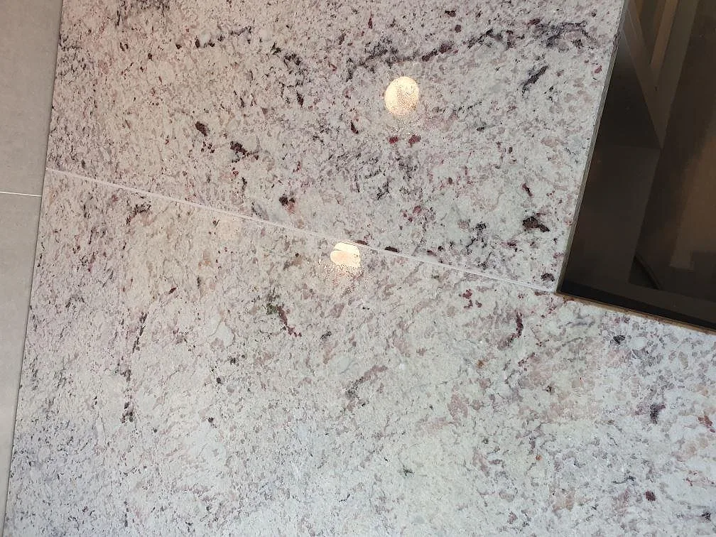 Detalj av polerad Antique White granit i Täby, med ljus yta, mörka mineralinslag och kant mot svart häll.