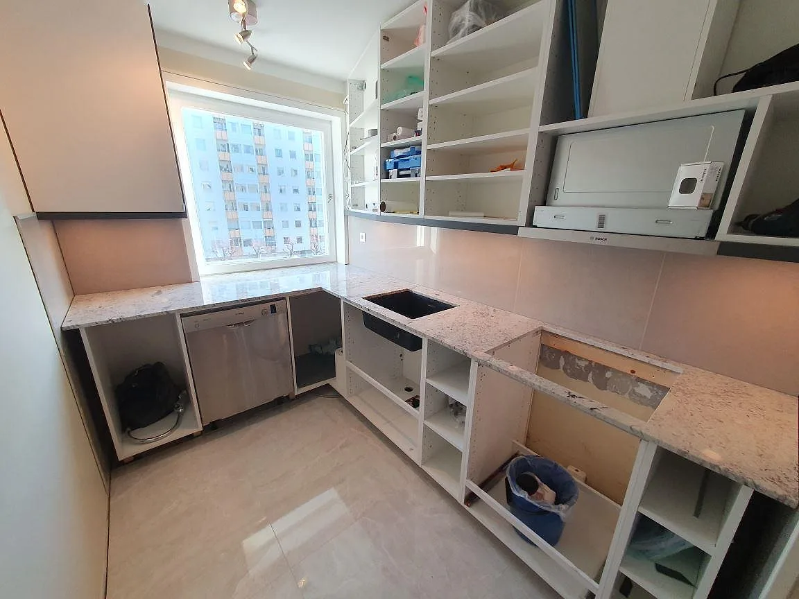Köksbänkskiva i Antique White granit under montering i Täby, med vit köksinredning och svart diskho.