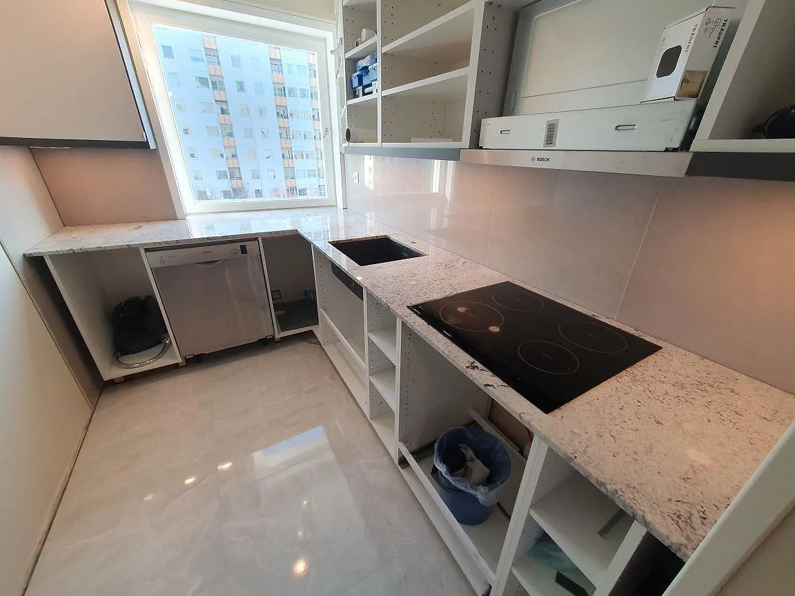 Köksbänkskiva i Antique White granit, polerad, i ett vinkelkök i Täby med induktionshäll ovanpå stenen och cremvit ådring.
