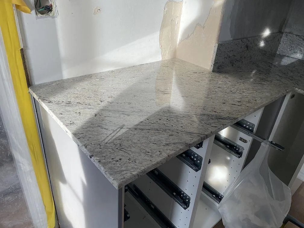 Lång köksbänkskiva i polerad Antique White granit på vita stommar under montering i Tomelilla.