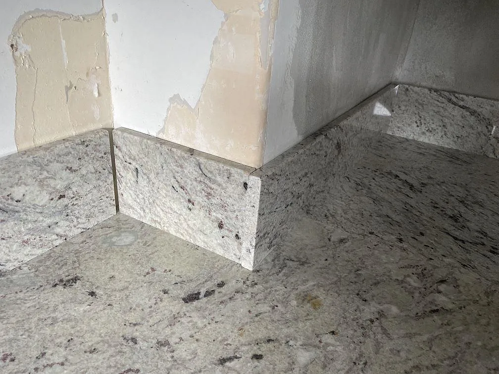 Detalj av Antique White granitbänkskiva med matchande stänkskydd och polerad naturstensyta i Tomelilla.