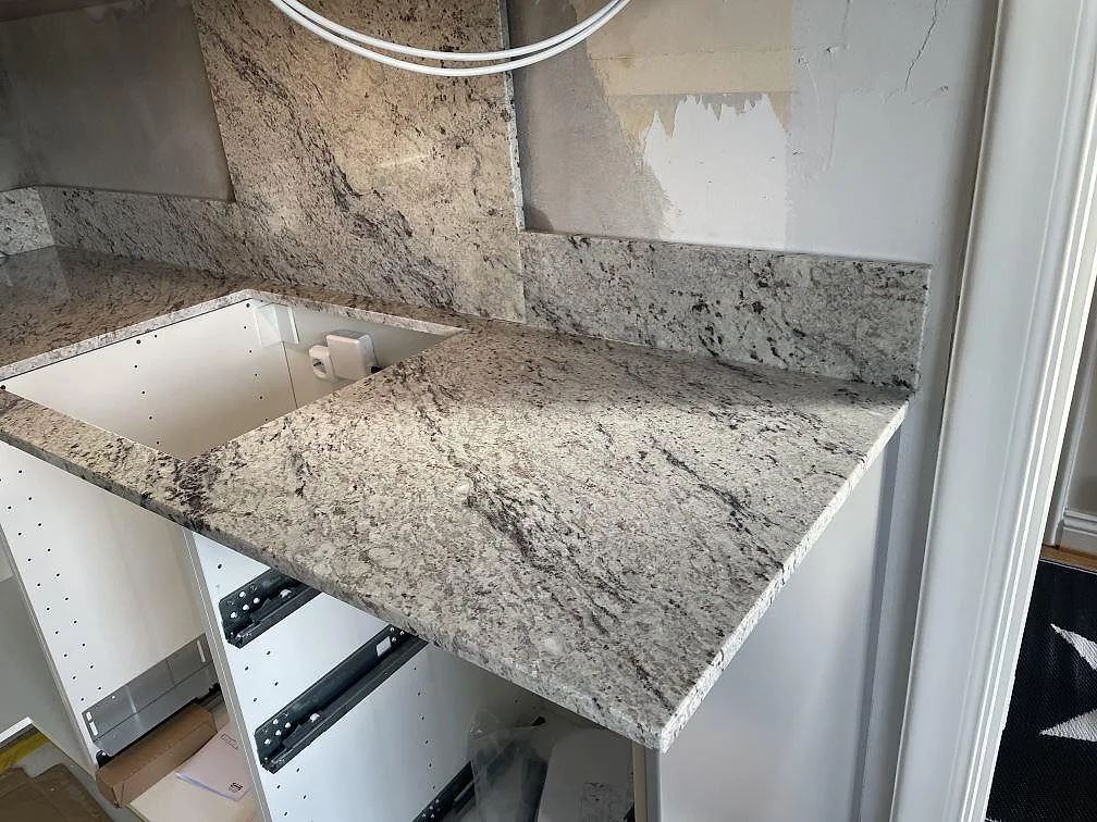 Köksbänk i Antique White granit med kort stänkkant och blank polerad yta i ett Tomelilla-kök.