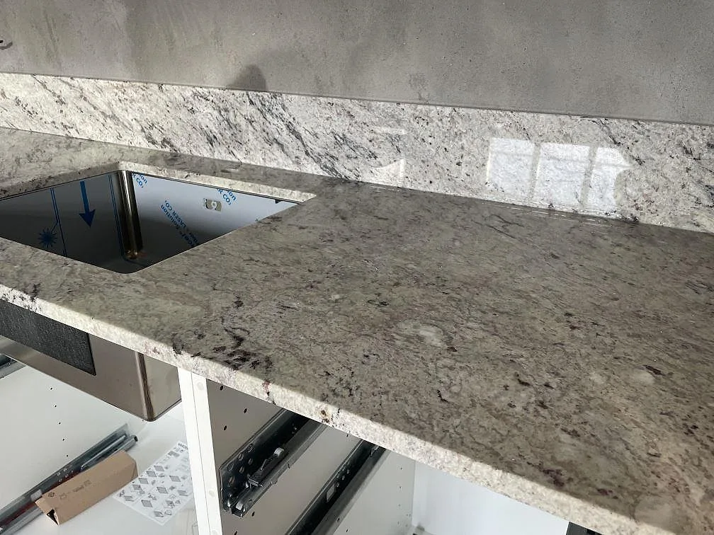 Köksbänkskiva i polerad Antique White granit med underlimmad rostfri diskho och stänkskydd i Tomelilla.