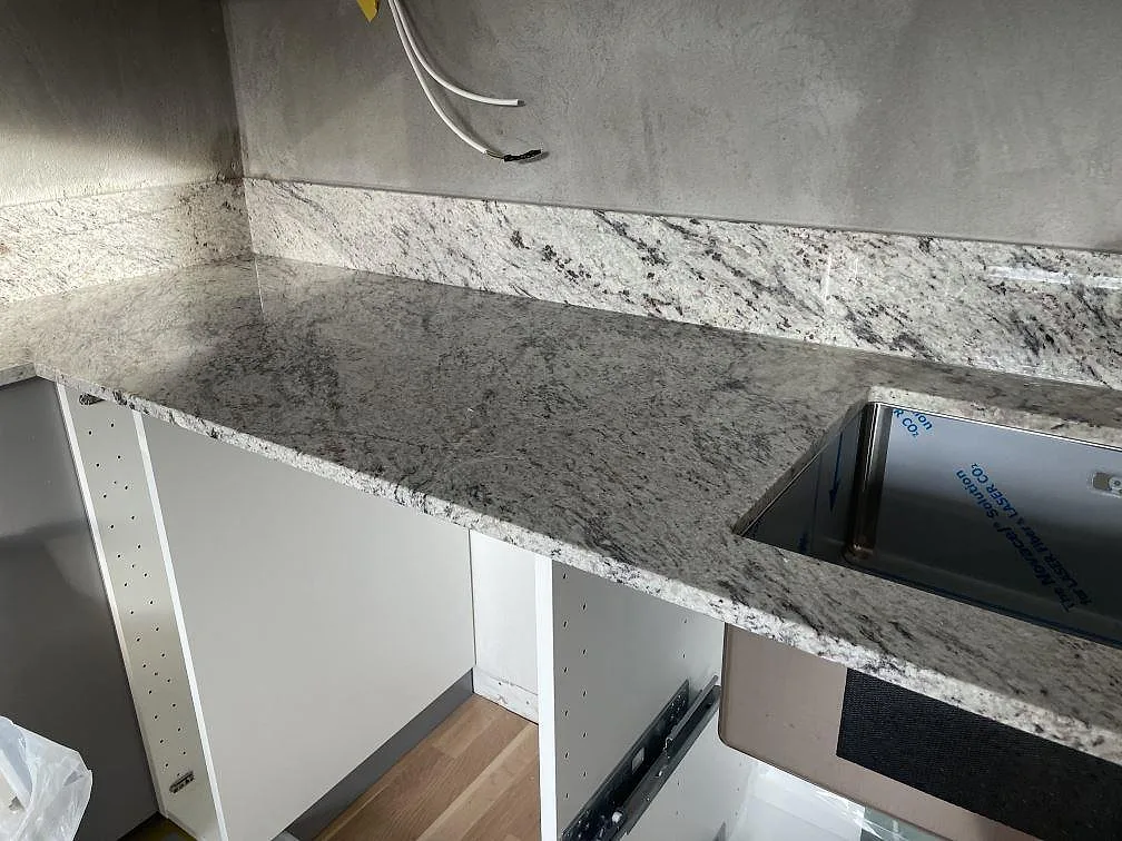 Polerad Antique White granitbänkskiva med rostfri diskho monterad under stenen i ett kök i Tomelilla.