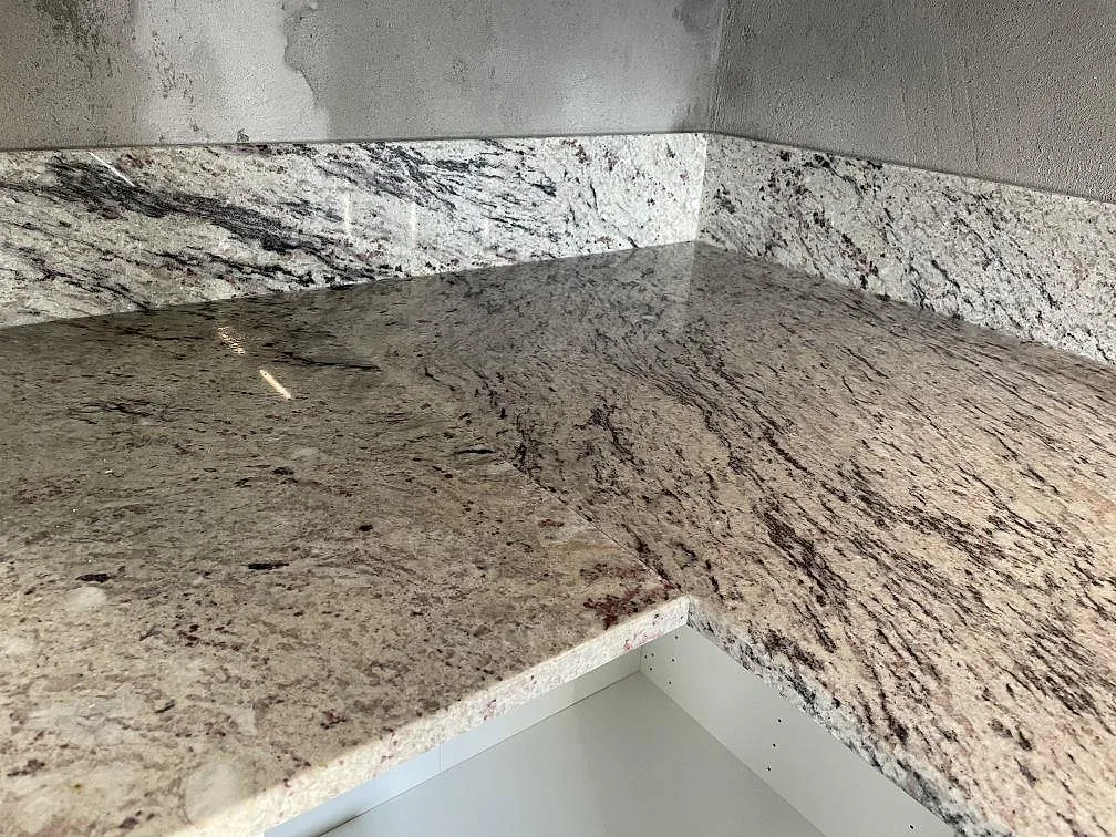 Närbild av polerad Antique White granit med ljus botten, mörk ådring och uppvikt stänkkant i Tomelilla.