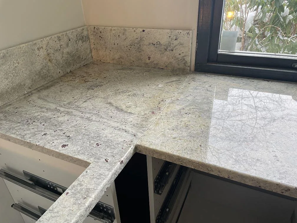 Hörnbänk i Antique White granit, polerad, med uppvikt stänkkant och tydlig grå ådring i ett kök i Trollhättan.