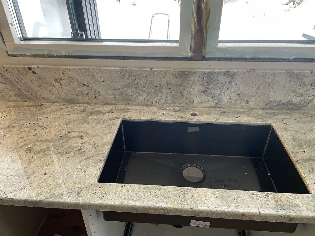 Underlimmad svart diskho i en köksbänkskiva av Antique White granit, polerad, i ett kök i Trollhättan.