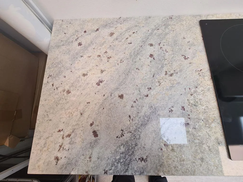 Närbild på polerad Antique White granit som köksbänkskiva vid den svarta induktionshällen i Uppsala.
