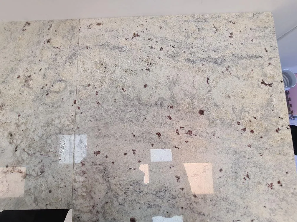 Närbild av installerad köksbänkskiva i polerad Antique White granit med skarv och blå köksinredning i Uppsala.