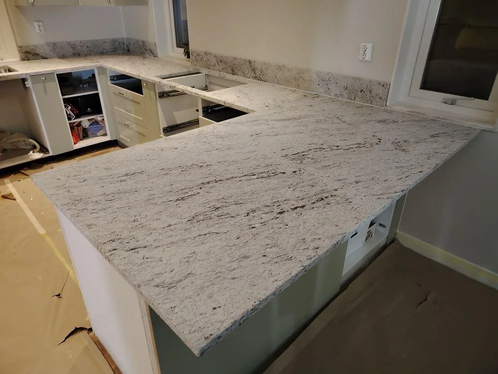 Närbild på stor köksyta i matt Antique White granit med mörk ådring och väggmonterad stänkkant i Västerås.