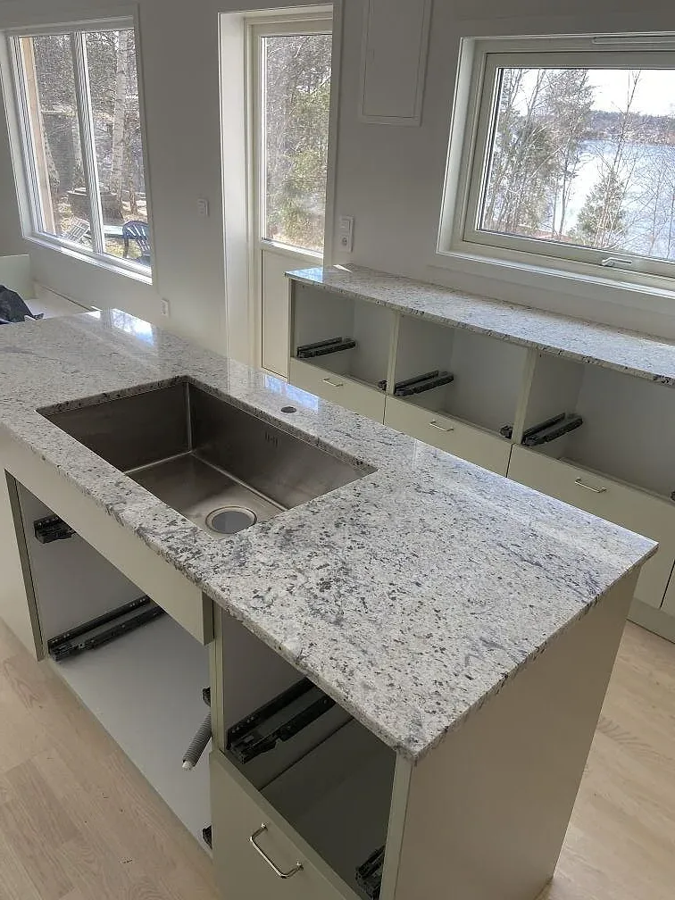 Köksö i polerad Antique White-granit med underlimmad rostfri diskho och stora fönster i ett kök i Växjö.