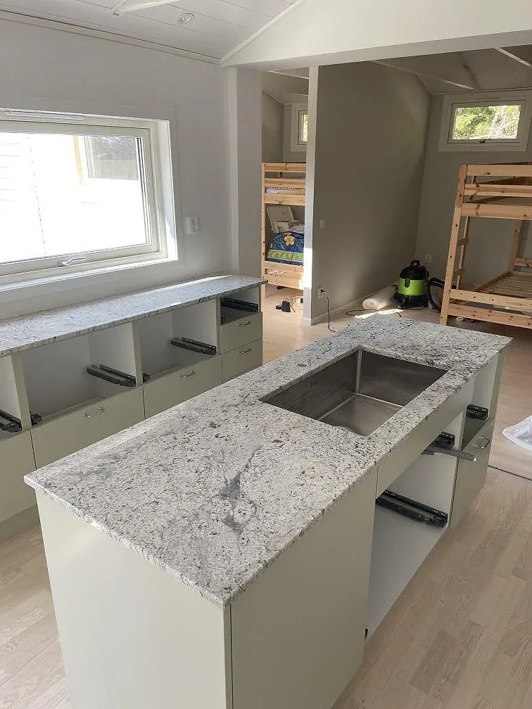 Köksö i Antique White-granit med urtag för underlimmad diskho, omgiven av köksstommar under montering i Växjö.