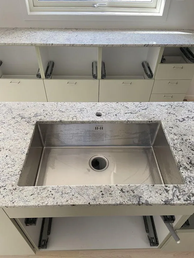 Närbild på underlimmad rostfri diskho i polerad Antique White-granit i ett kök i Växjö.