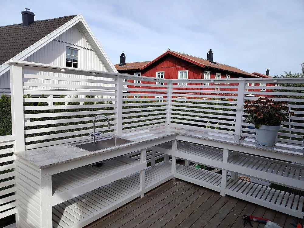 Utekök med bänkskiva i polerad Antique White granit, underlimmad rostfri diskho och vit trästomme på ett trädäck i Vendelsö.