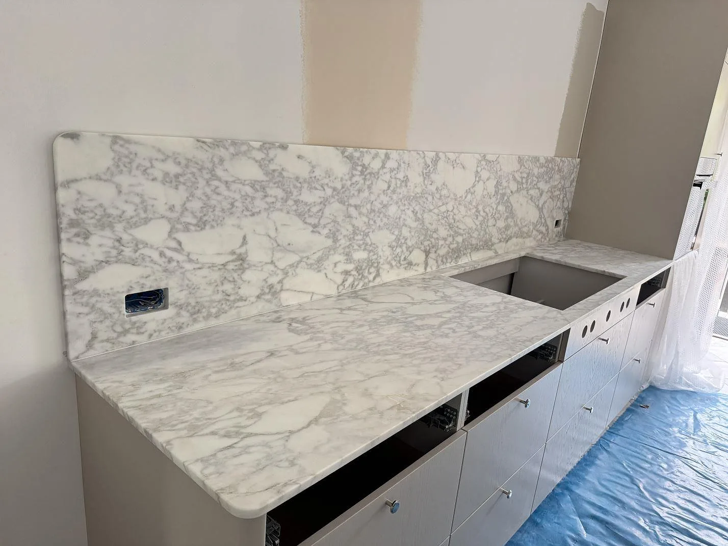 Köksbänkskiva i matt Arabescato marmor med stänkskydd och hällurtag i ett kök i Charlottenlund.