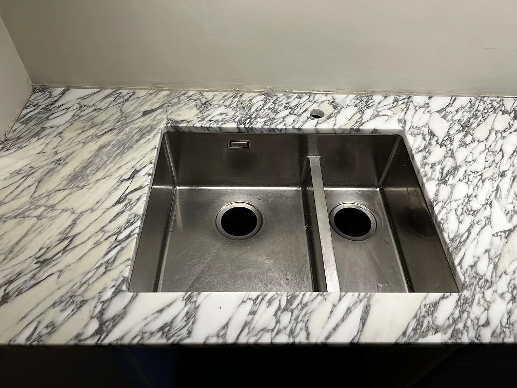 Underlimmad rostfri dubbelho i en köksbänkskiva av matt Arabescato marmor i Göteborg.