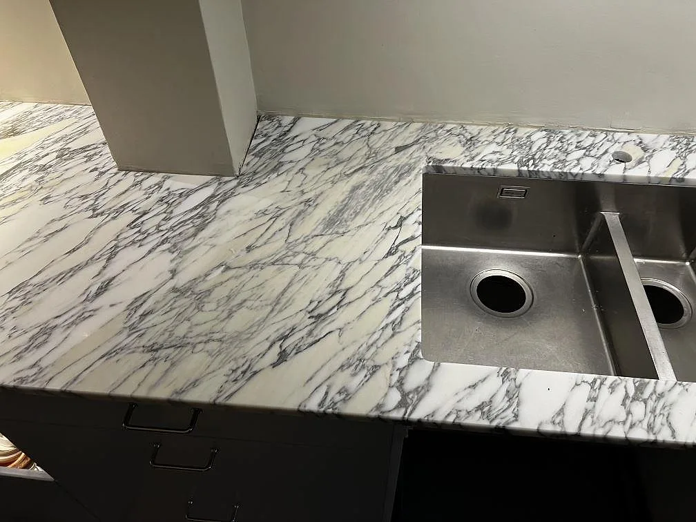 Detalj av Arabescato marmor runt den rostfria dubbelhon, matt yta och kraftig grå ådring i Göteborg.