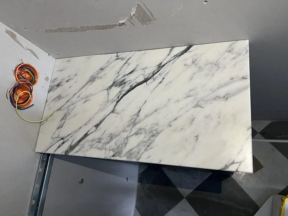 Rak bänkskivedel i matt Arabescato marmor monterad mot vägg i kök under arbete i Lidingö.