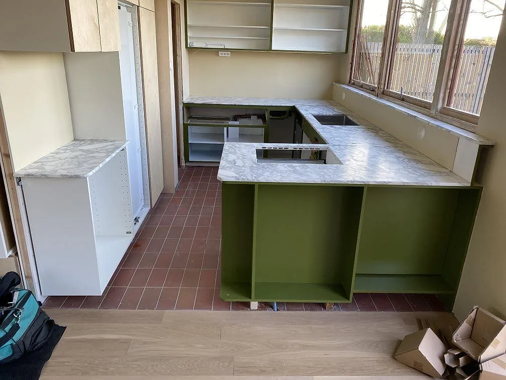 Köksbänkskiva i matt Arabescato-marmor med halvö, hällöppning och uppvikta stänkkanter i ett kök under montering i Limhamn.
