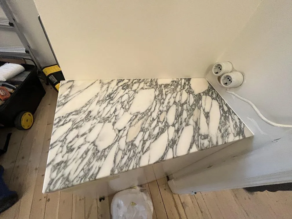 Fristående köksdel med vattenfallssida i matt Arabescato marmor och kraftig grå ådring under montering i Stockholm.