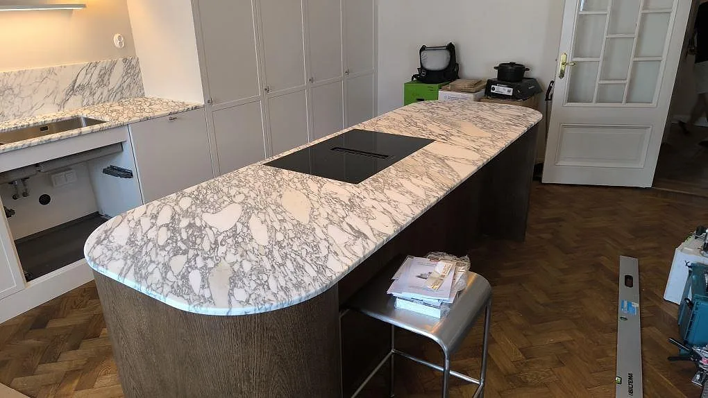 Köksö i matt Arabescato marmor med infälld häll och rundad kortsida i ett kök i Stockholm.