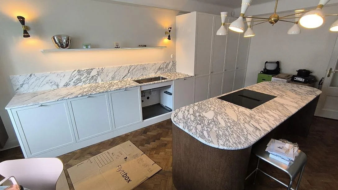 Köksbänkskiva och köksö i matt Arabescato marmor, med häll och stänkskydd i ett kök i Stockholm.
