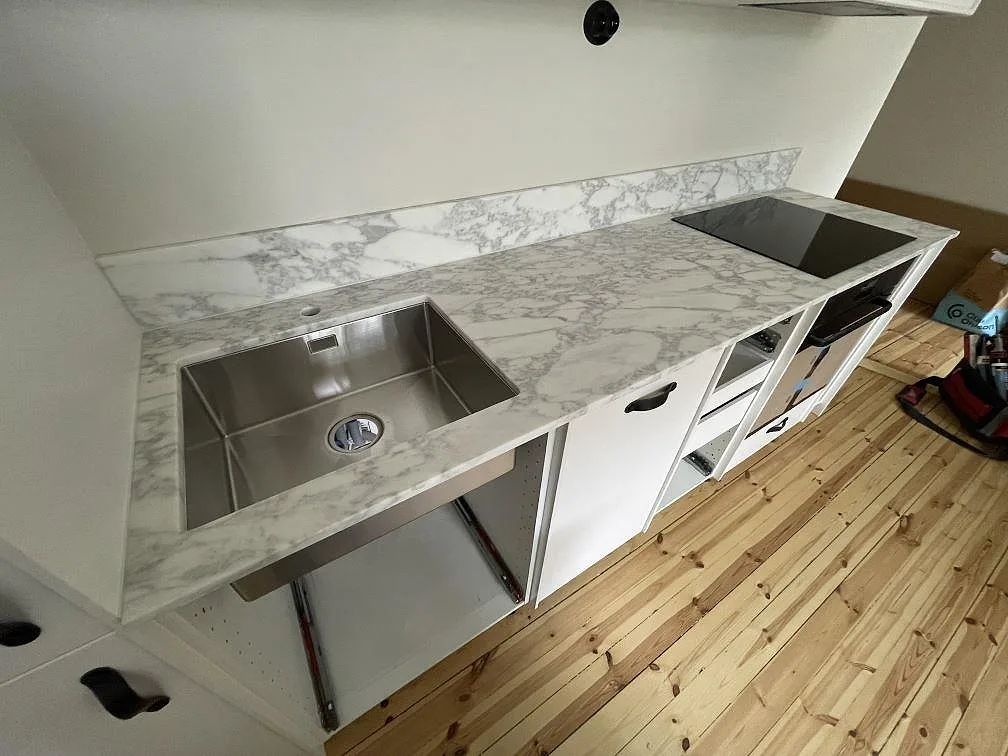 Matt Arabescato-marmor som köksbänk med diskhoområde, svart häll och stänkkant på vita köksstommar i Stockholm.