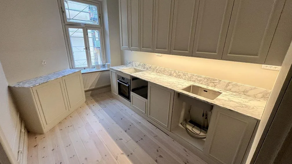 Vägggående bänkskiva i Arabescato marmor, matt, med synlig diskho och stänkkant över beige köksskåp i Stockholm.