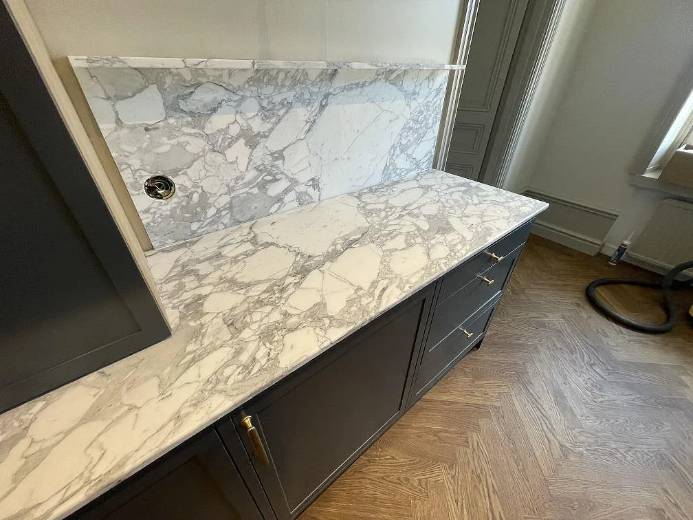 Detaljbild av gråvit ådring i matt Arabescato marmor på bänkskiva och stänkskydd i Stockholm.