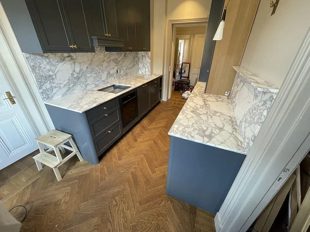 Köksbänkskiva i matt Arabescato marmor, 20 mm, med matchande stänkskydd och flera arbetsytor i ett kök i Stockholm.