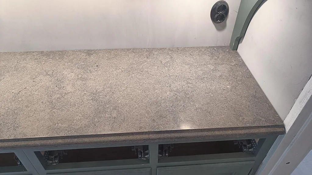 Installerad köksbänkskiva i matt Azul Valverde-marmor på sagegröna stommar med synlig stenstruktur i Barsebäck.