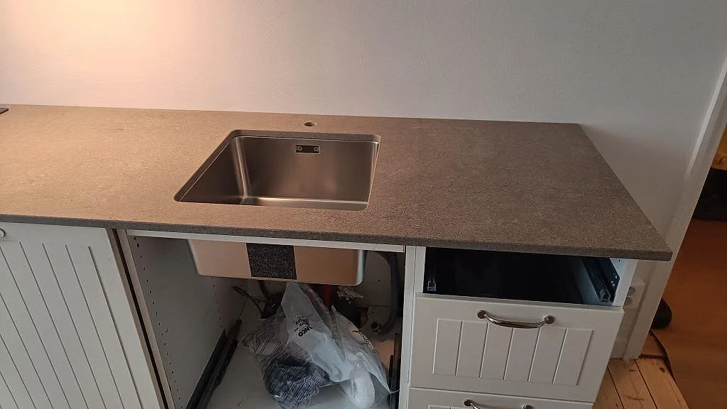 Installerad köksbänkskiva i matt Azul Valverde marmor med rostfri diskho och synlig grå stenyta under montering i Göteborg.
