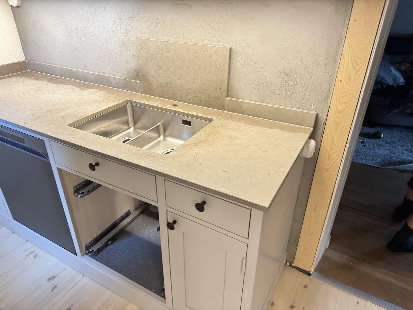Köksbänkskiva i Azul Valverde, matt gråbeige marmor, med diskho och låg stänkkant i ett kök under montering i Höör.