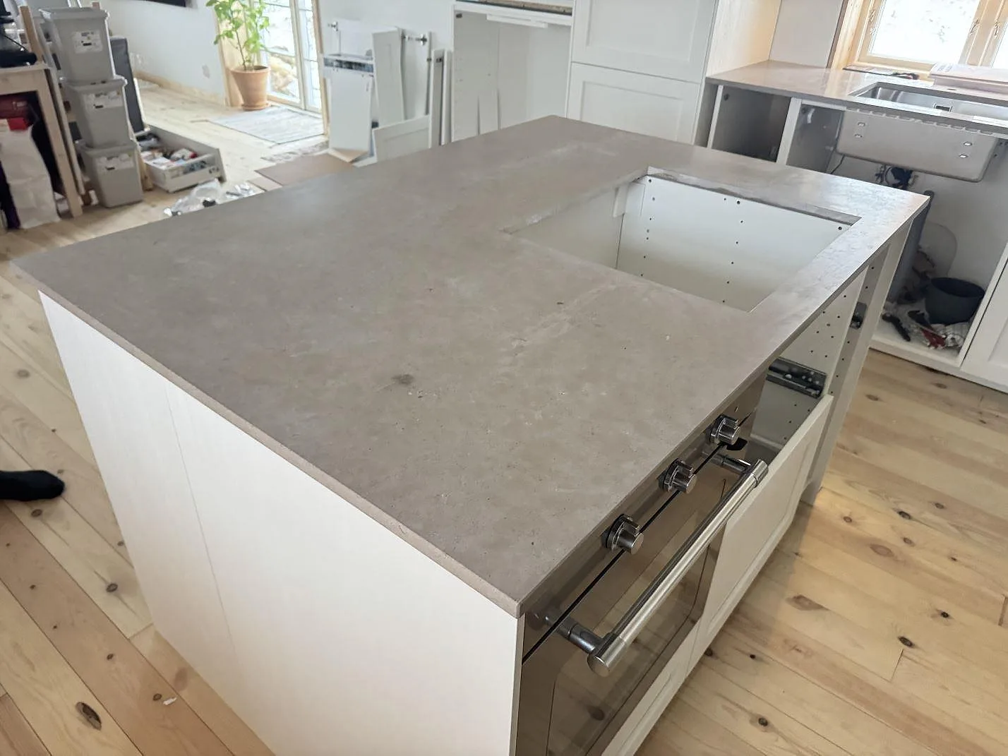 Fristående köksö i matt Azul Valverde med en separat bänkrad längs fönstret i ett kök under montering i Kristianstad.