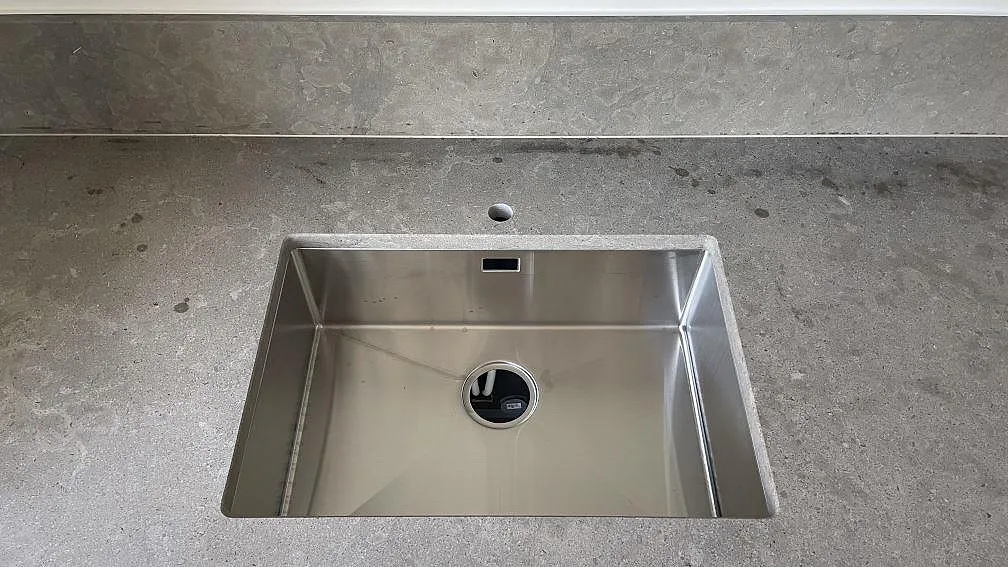 Underlimmad rostfri diskho infälld i grå Azul Valverde kalkstensbänk, sedd ovanifrån i ett kök i Malmö.