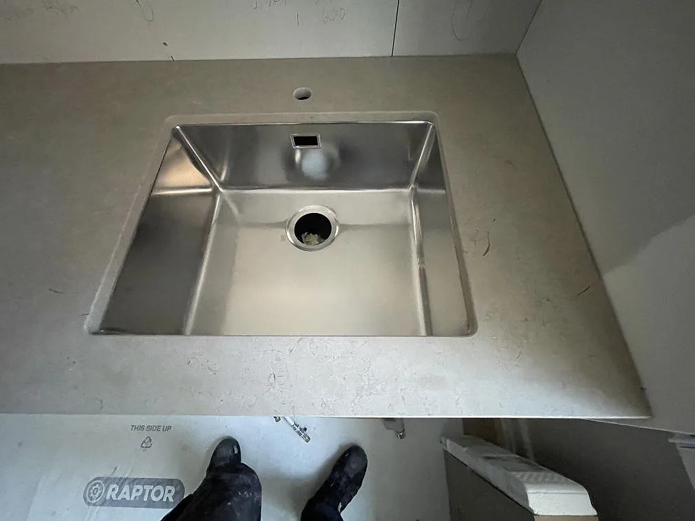 Underlimmad rostfri diskho infälld i matt Azul Valverde bänkskiva, sedd uppifrån med stenens fossila ådring, i ett kök i Stockholm.