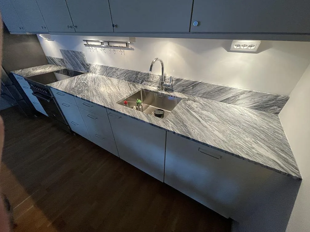 Köksbänkskiva i grå Bardiglio marmor i ett kök i Stockholm, med underlimmad rostfri diskho, blandare och uppvikt stänkskydd i samma sten.