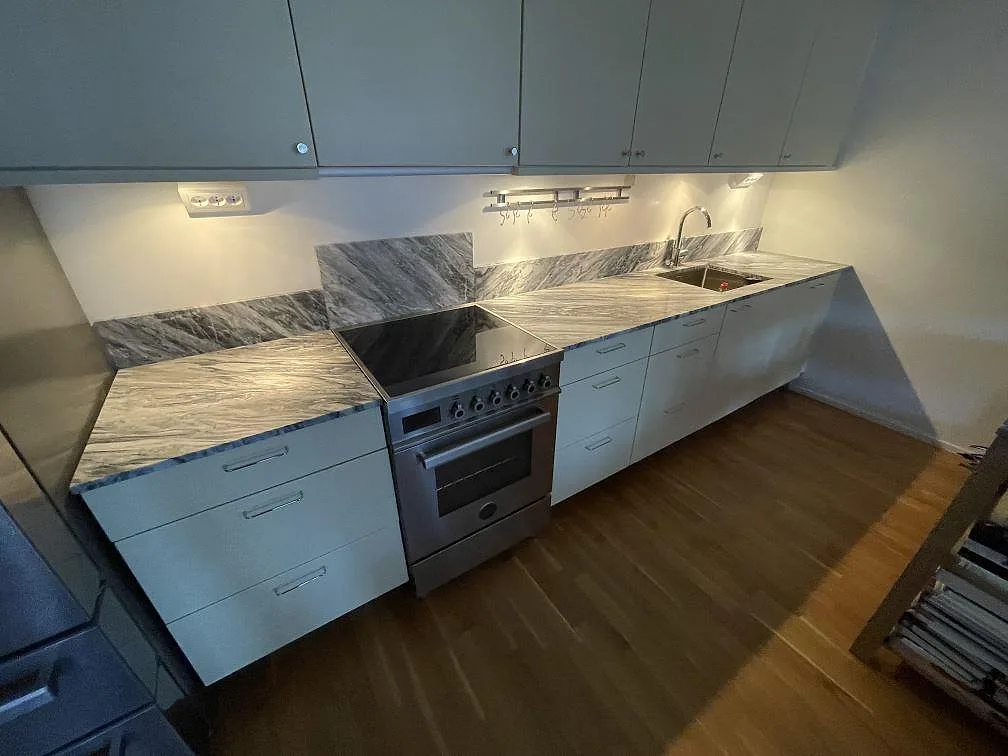 Köksbänkskiva i grå Bardiglio marmor, matt yta, med induktionshäll och underlimmad rostfri diskho längs en köksrad i Stockholm.