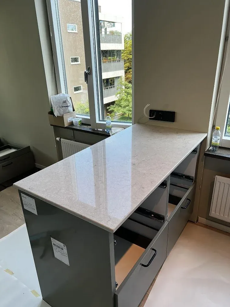 Köksö i polerad Bianco Drift komposit framför stora fönster under montering i ett kök i Limhamn.