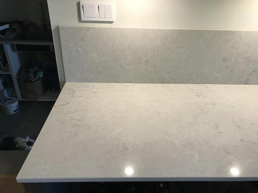 Bianco Drift köksbänkskiva med mjuk grå ådring och uppvikt stänkkant i ett kök i Lomma.