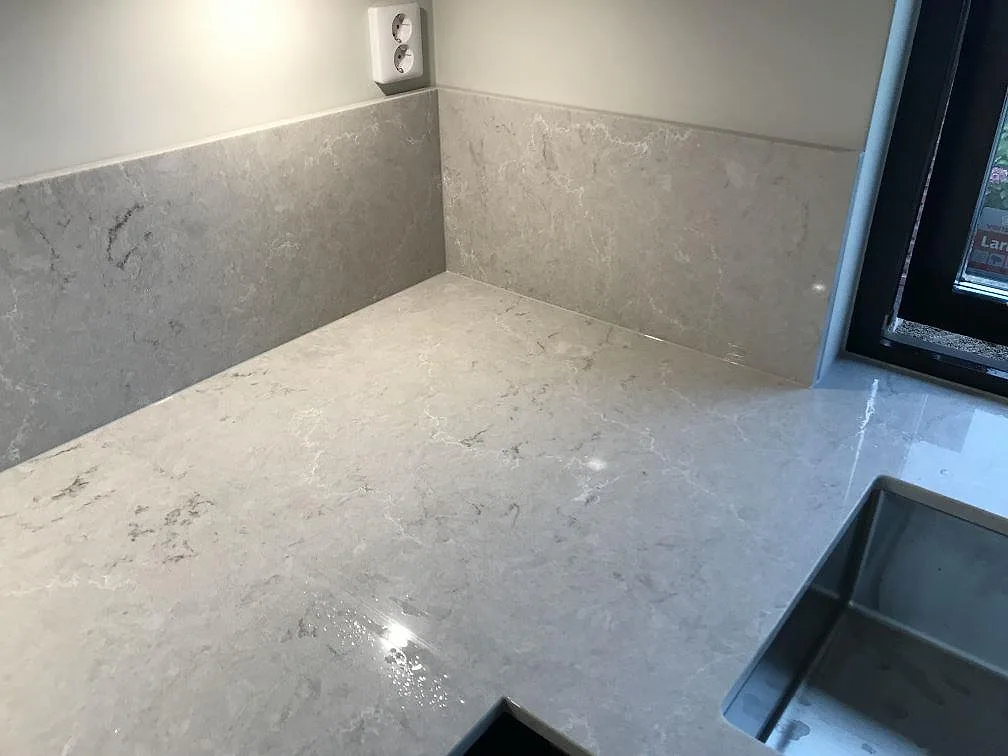 Bianco Drift köksbänkskiva med uppvikt stänkkant och underlimmad rostfri diskho i ett hörn av köket i Lomma.