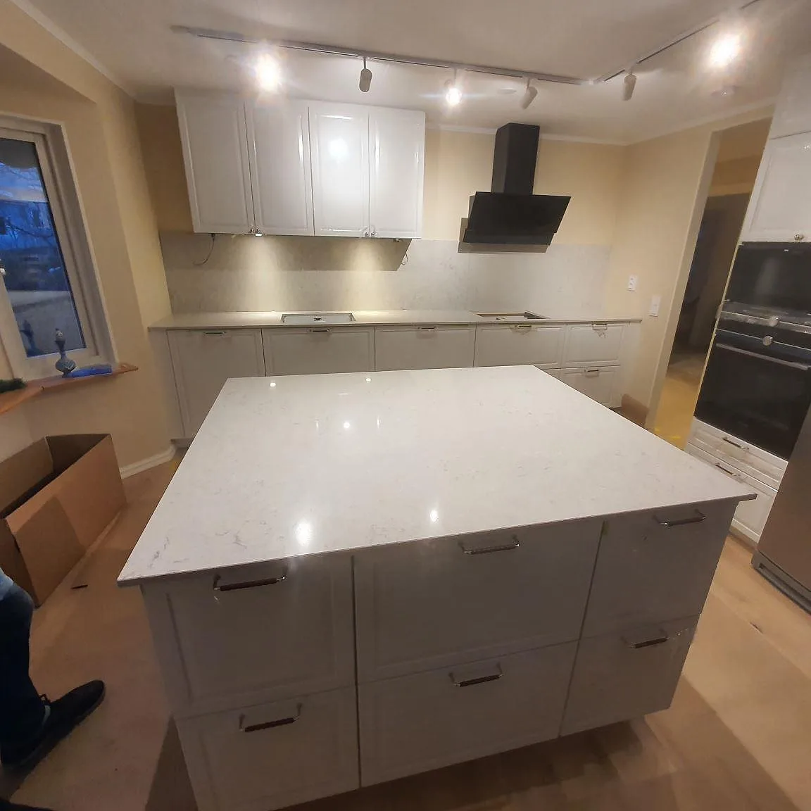 Köksbänkskiva och köksö i vit Caesarstone Bianco Drift komposit, polerad, med uttag för häll och diskho i ett kök i Sollentuna.