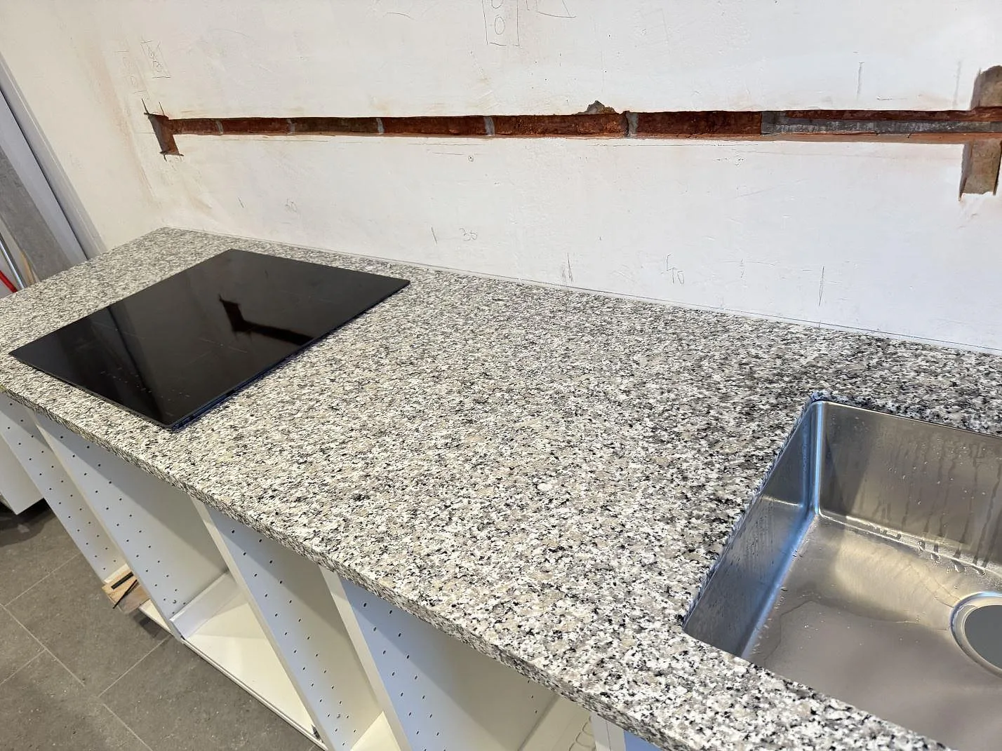 Polerad köksbänkskiva i Bianco Sardo granit med häll, diskho och öppen skåpsstomme i ett kök i Helsingborg.