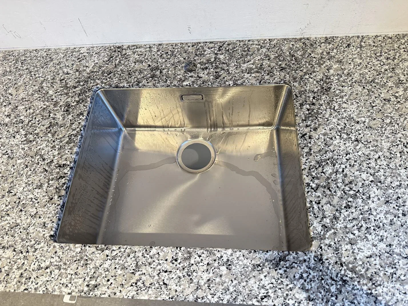 Närbild på polerad Bianco Sardo granit runt rostfri diskho i en köksbänkskiva i Helsingborg.