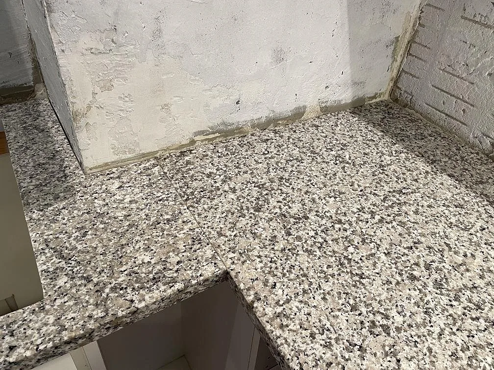 Hörnparti av polerad Bianco Sardo granitbänkskiva mot rå betongvägg i ett kök i Lund.