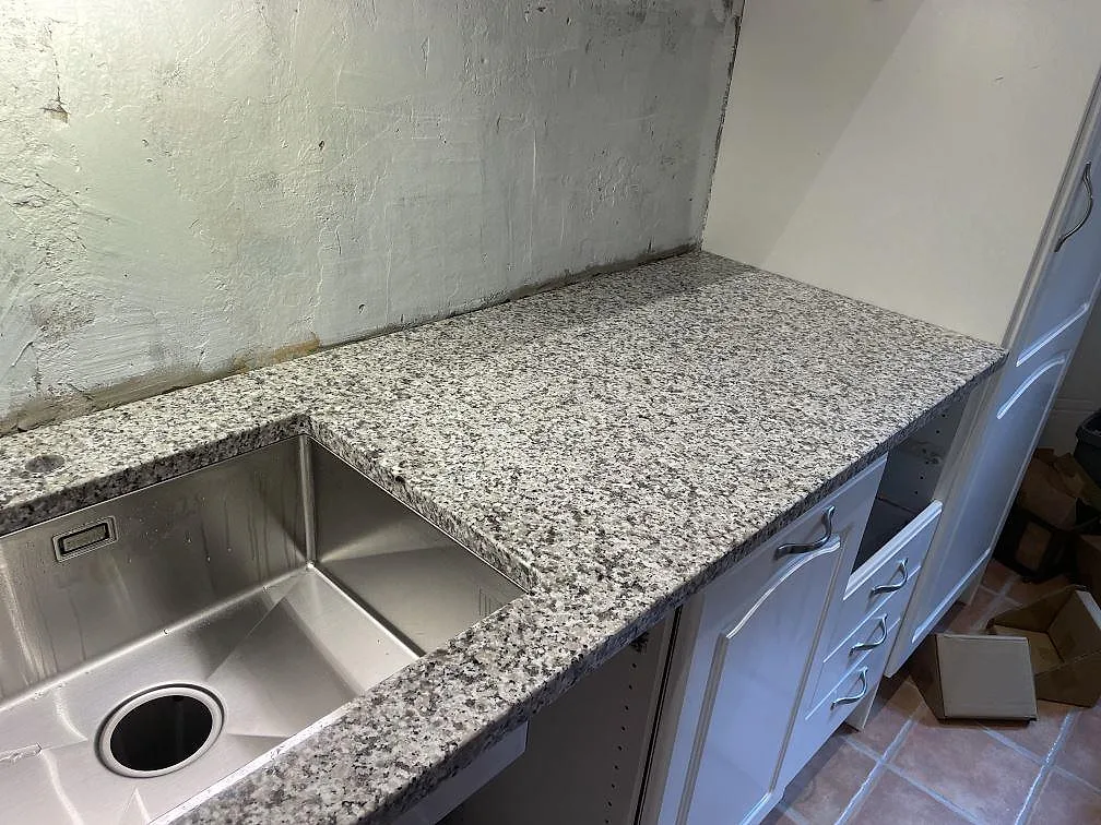 Polerad Bianco Sardo granitbänkskiva med underlimmad rostfri diskho och vita ramluckor i ett kök i Lund.