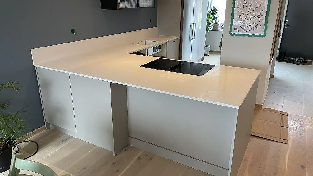 Stor köksö och köksbänkskiva i polerad Blanco Norte komposit med häll och diskho i ett kök i Helsingborg.